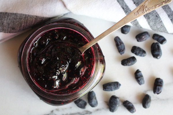 Homemade honeyberry jam (Haskap Jam) without pectin sits on a marble countertop, open and with a spoon in the jar