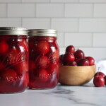 Two pint jars of home canned crabapples on a white counter with a bowl of crabapples next to them.