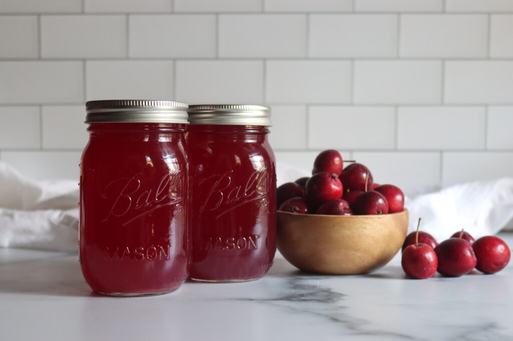 Crabapple Juice in jars on a counter next to red crabapples.