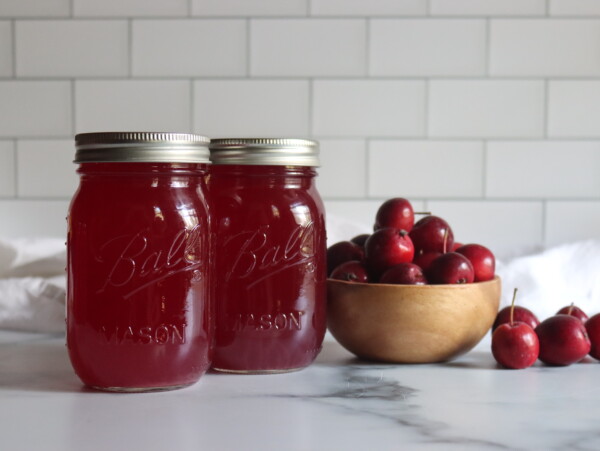 Crabapple Juice in jars on a counter next to red crabapples.