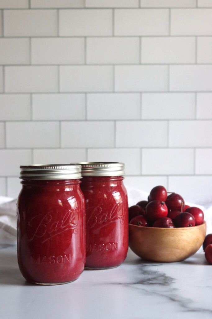Two jars of crabapple sauce on a white countertop.