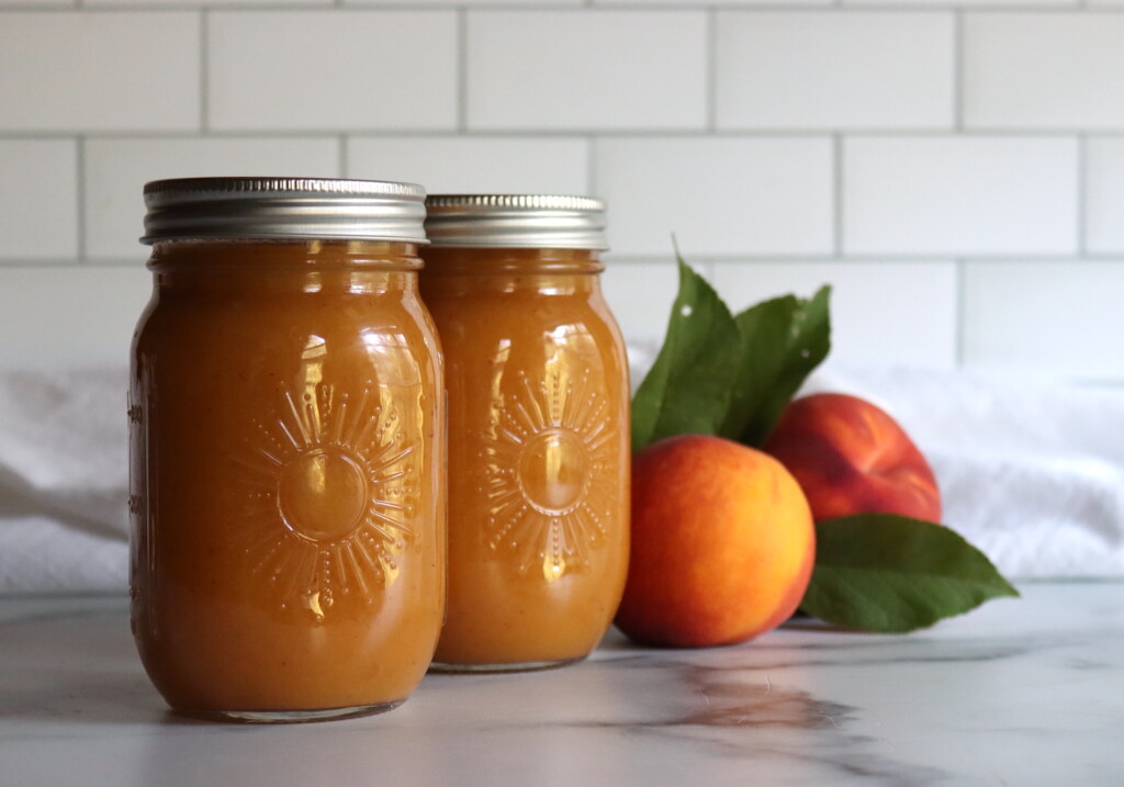Two jars of peach nectar in sunshine jars on a white counter.