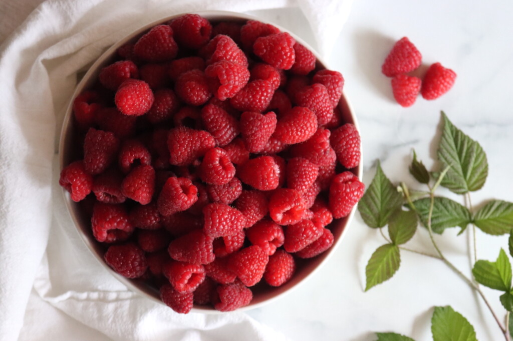 A bowl of raspberries on a white surface.