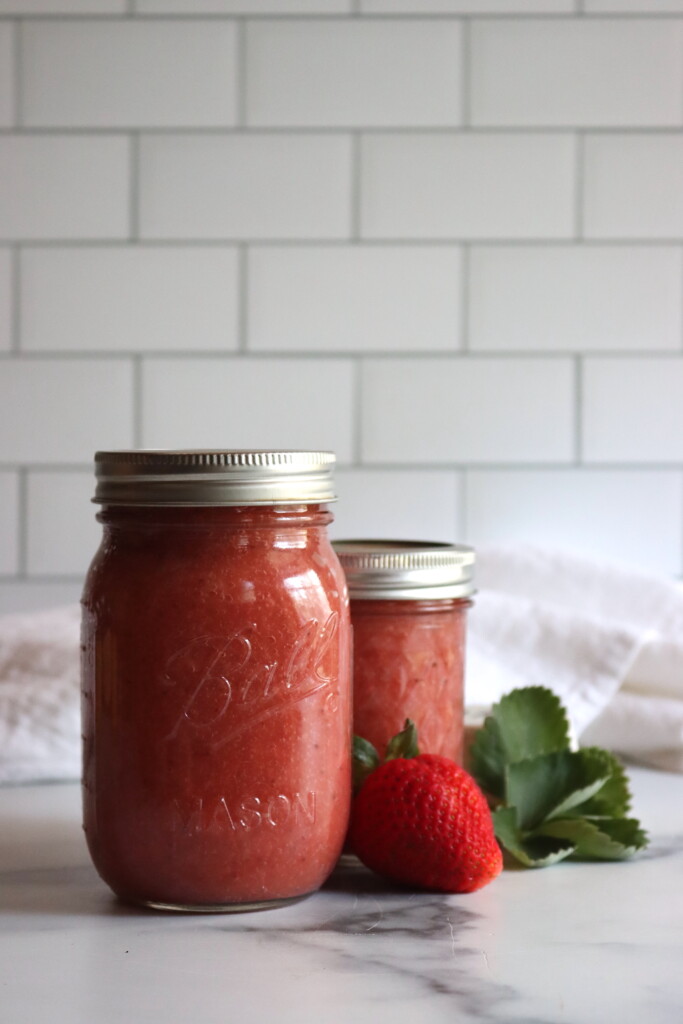 Strawberry Applesauce in two canning jars on a white surface.