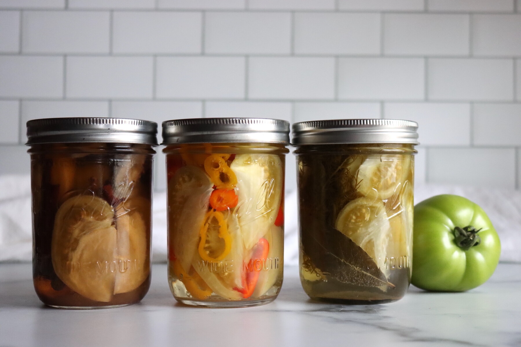 Three different pickled green tomato recipes, from left to right: Sweet, Spicy and Dill.