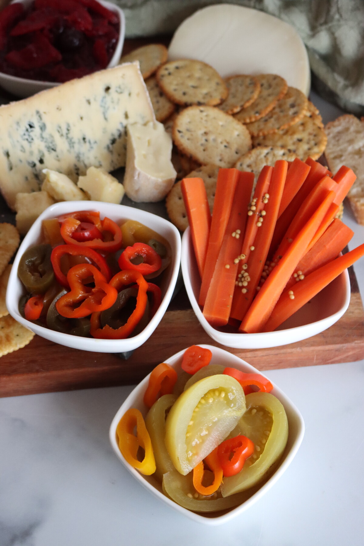 Spicy pickled green tomatoes served on a cheese board with sweet pickled carrots and pickled peppers.