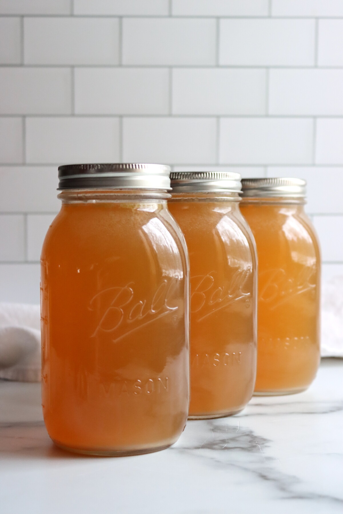 Three quart jars of pressure canned turkey stock on a white counter.