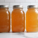 Three jars of turkey broth in a line on a white counter.