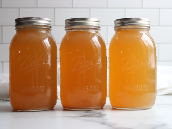 Three jars of turkey broth in a line on a white counter.