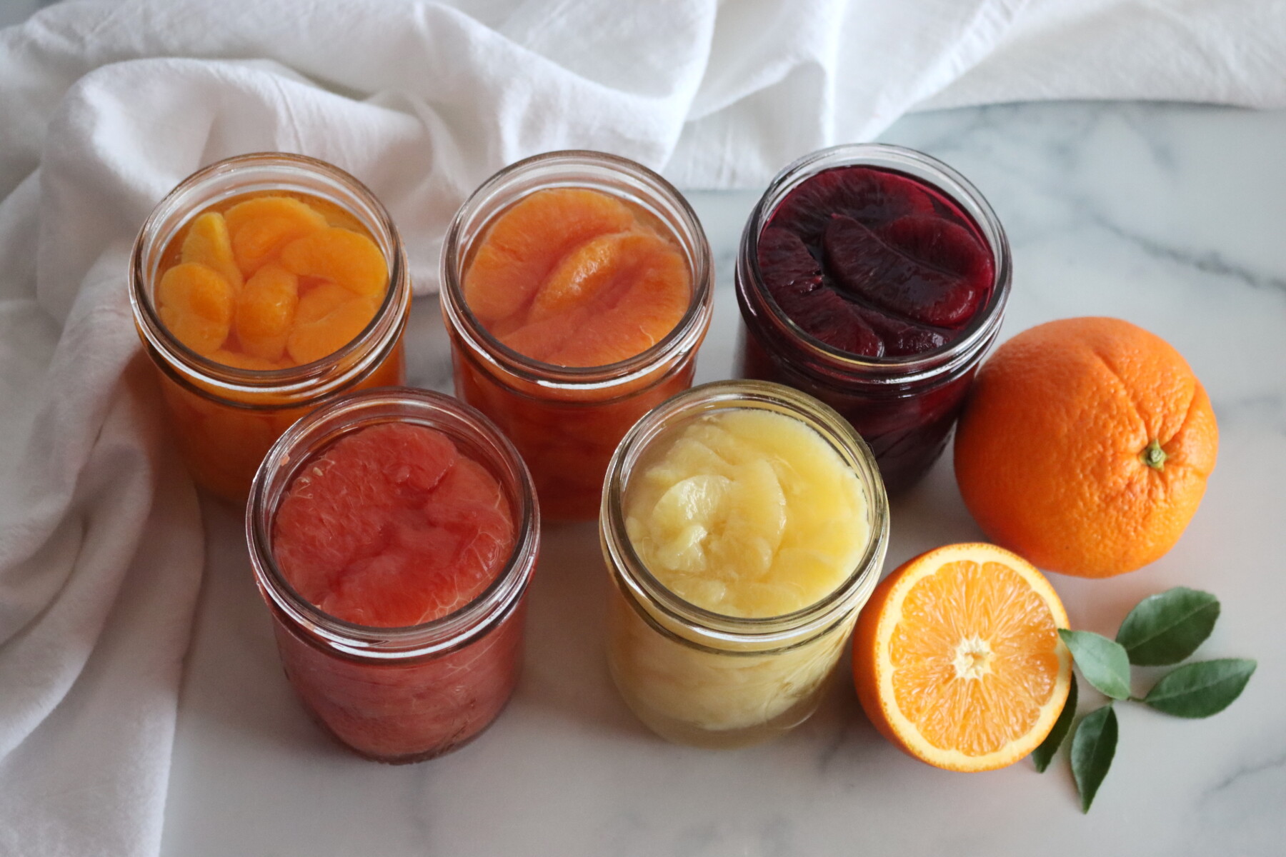 Jars of Canned citrus segments.  From Left to right: Mandarins, cara cara oranges, blood oranges, grapefruit and lemons.