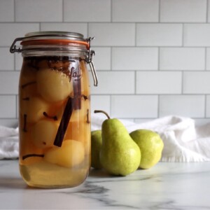 Homemade pickled pears in a jar on a white countertop.