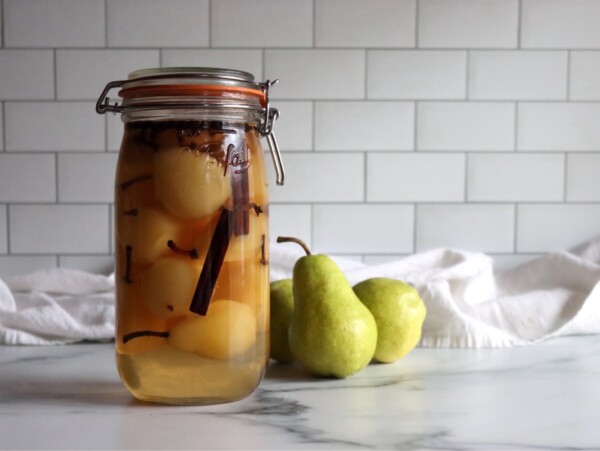 Homemade pickled pears in a jar on a white countertop.
