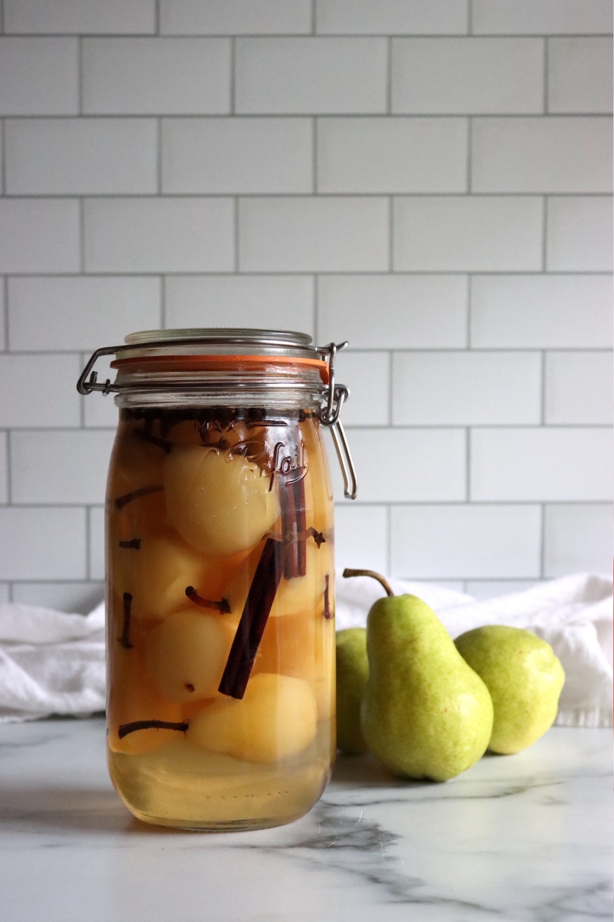 Pickled pears in a jar on a white table.