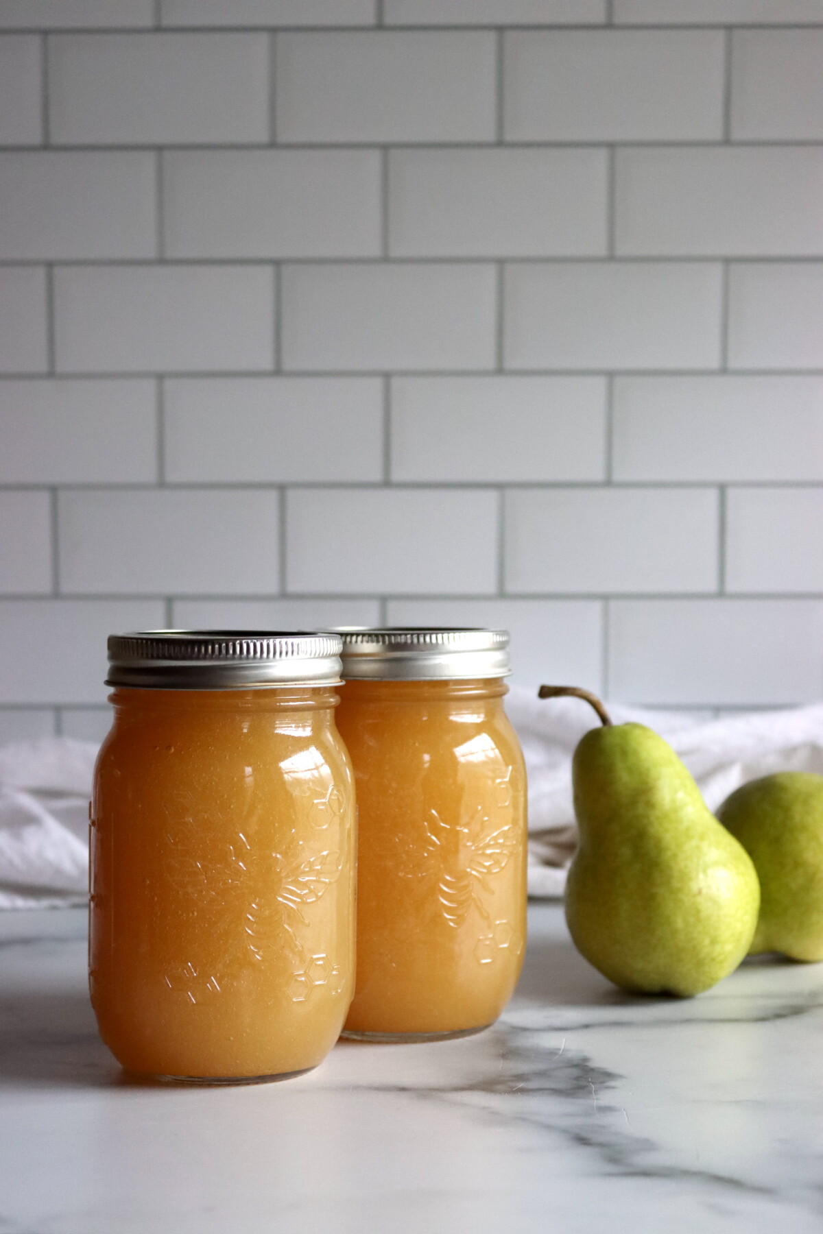 Two pint jars of homemade pear honey beside fresh pears
