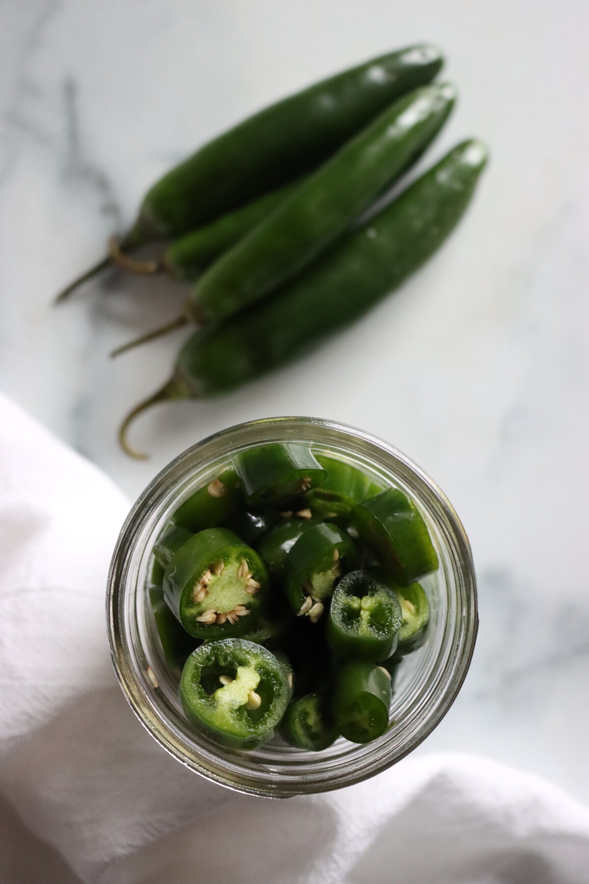 Serrano pepper rings packed in an open jar, seen from above, next to fresh serrano peppers