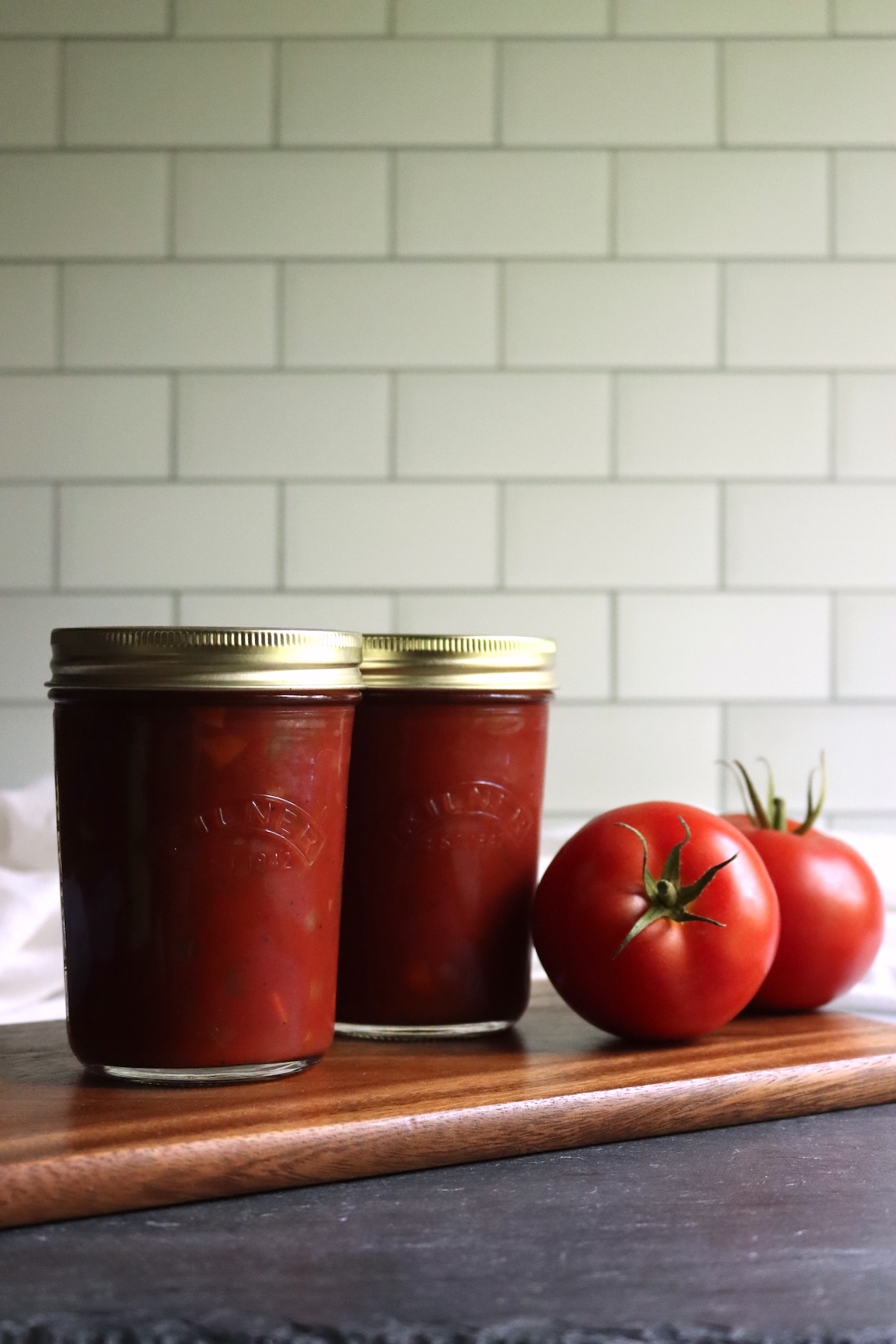 Two pints of home-canned Italian-style tomato sauce next to fresh tomatoes