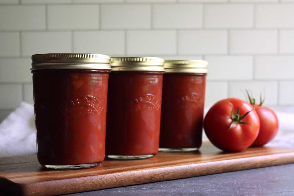 Three jars of Italian-style tomato sauce in a row on a wooden board with fresh tomatoes