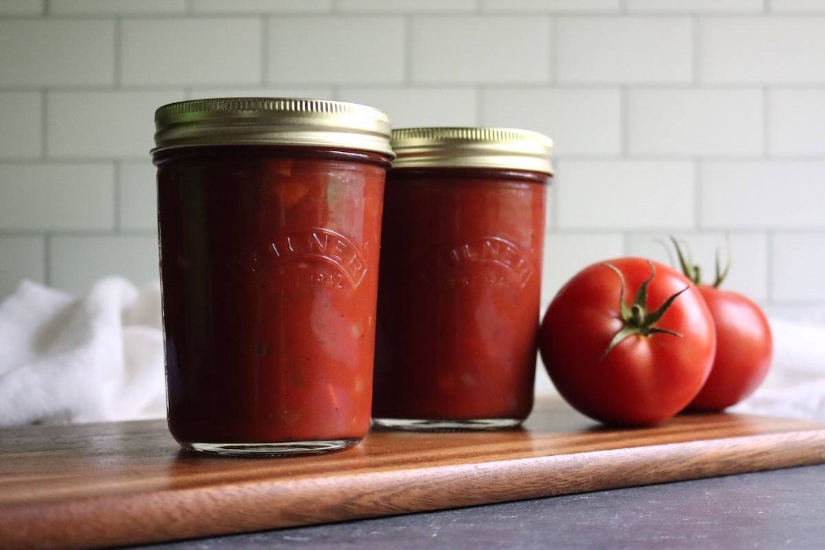 Two jars of Italian-style tomato sauce on a wooden board with fresh tomatoes