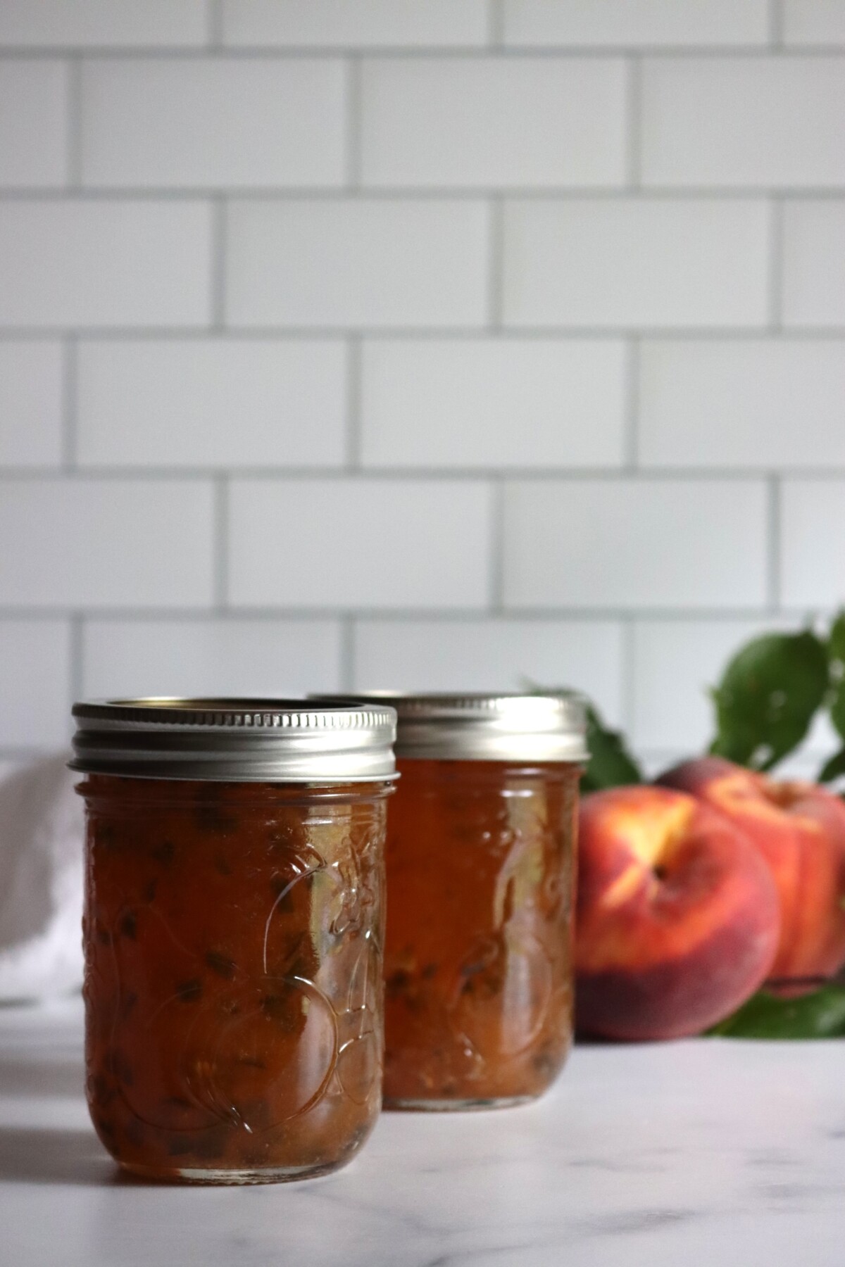 Peach jalapeño jam in half-pint jars with a halved peach behind them