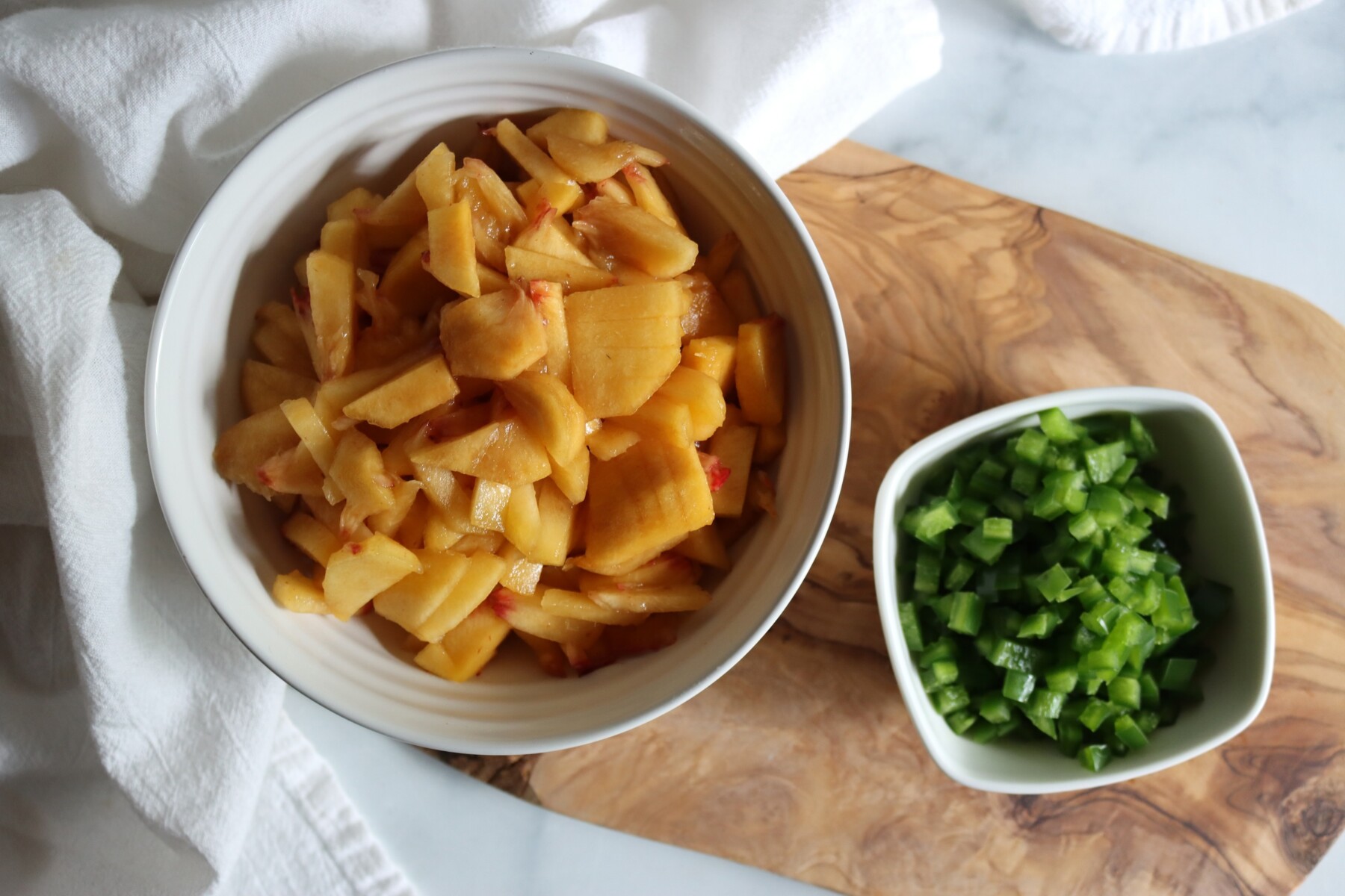 Chopped peeled peaches and finely chopped jalapeños in bowls, ready for peach jalapeño jam