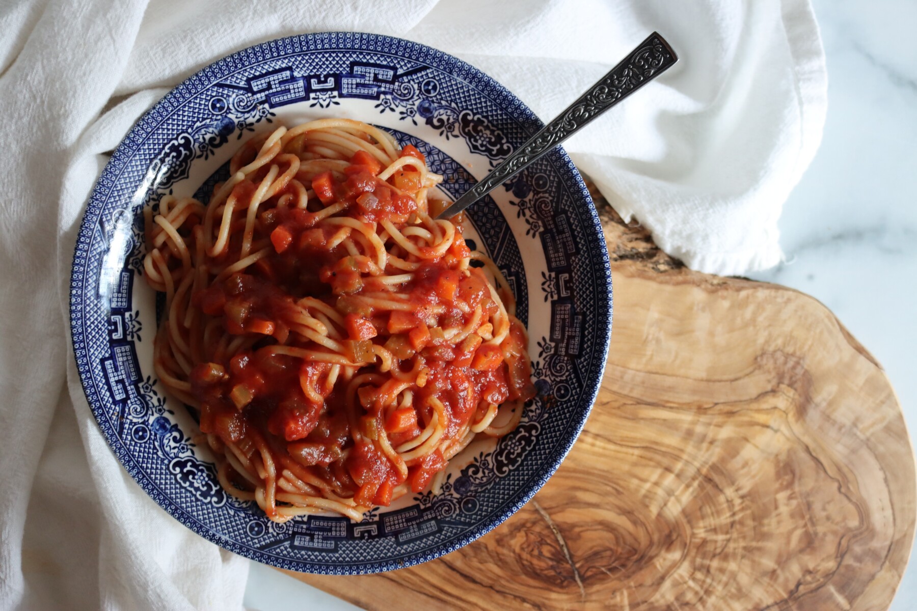 Spaghetti with homemade Italian tomato sauce in a blue and white bowl on an olive wood board