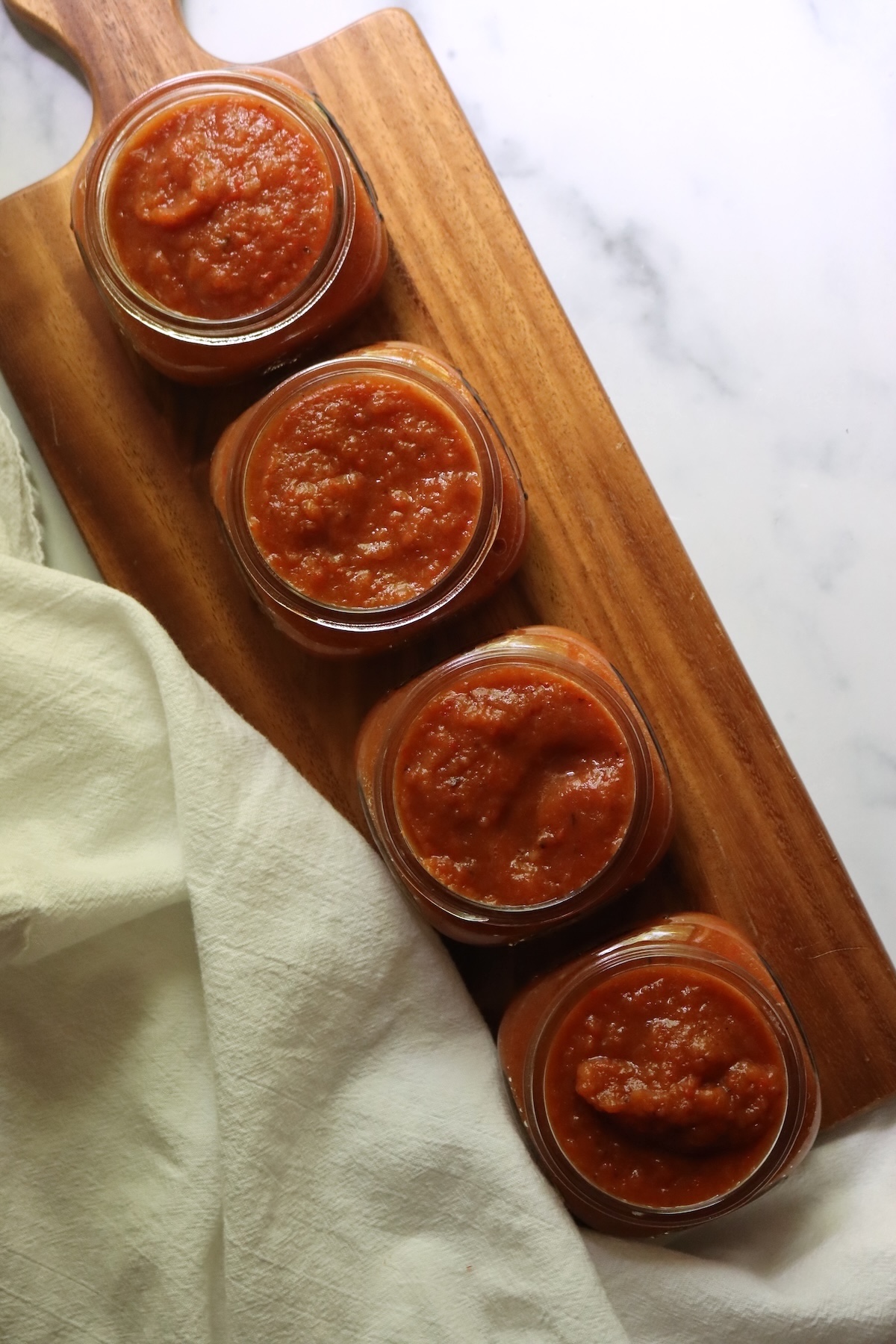 Four half-pint jars filled with ajvar, lined up on a wooden board