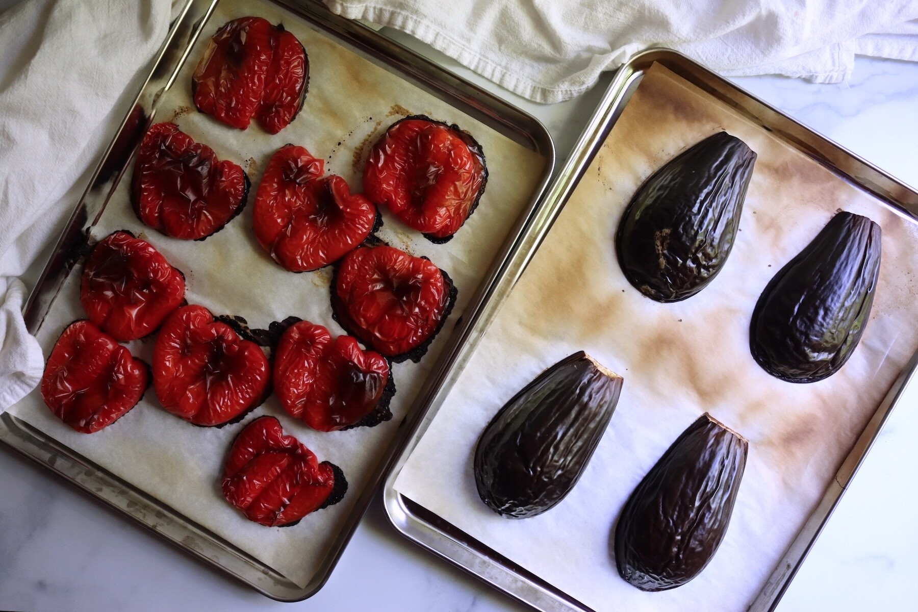 Red bell pepper halves and eggplant halves roasted skin side up on two parchment-lined baking sheets
