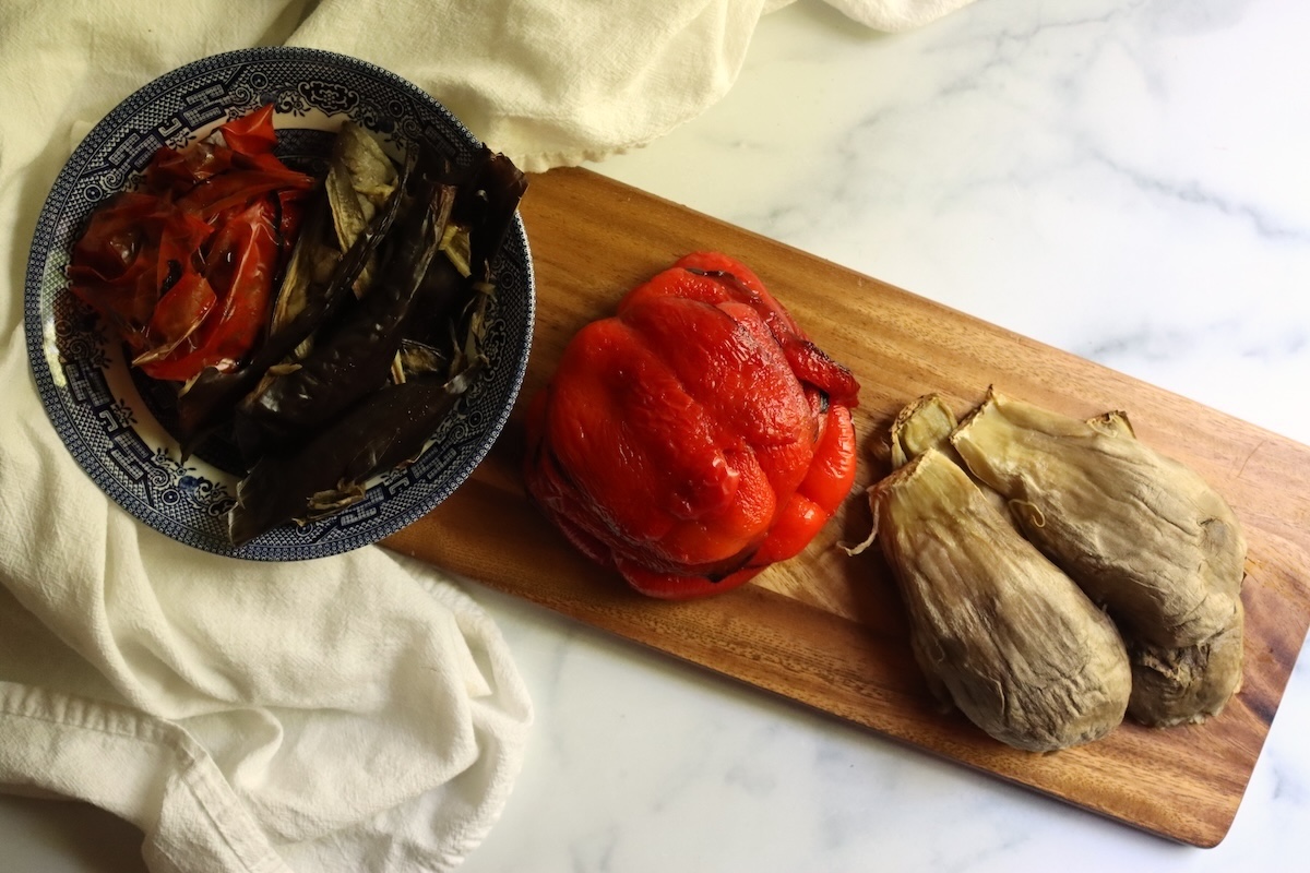 Peeled roasted red peppers and scooped eggplant on a cutting board, with the skins in a bowl