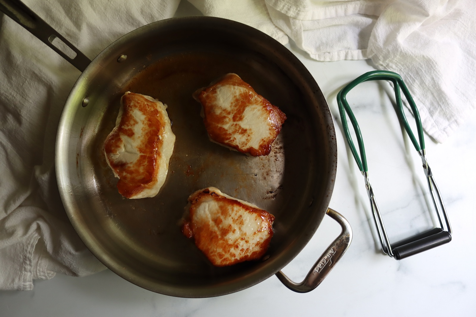 Browning pork chops in a stainless steel skillet for hot pack canning