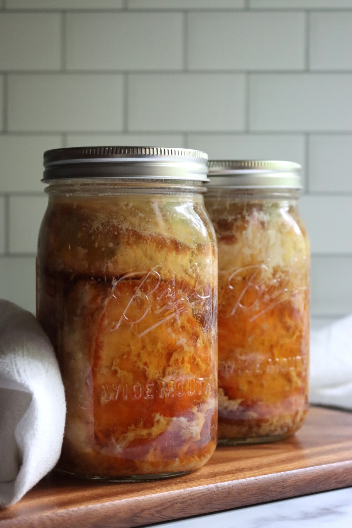 Two jars of canned pork chops in broth beside a white kitchen towel