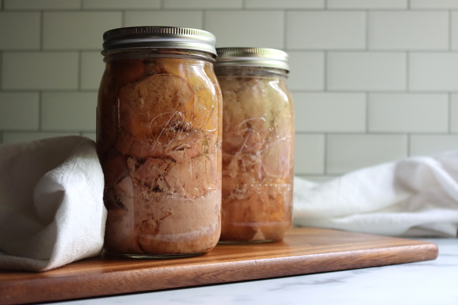 Two quart jars of home-canned pork tenderloin on a wooden cutting board