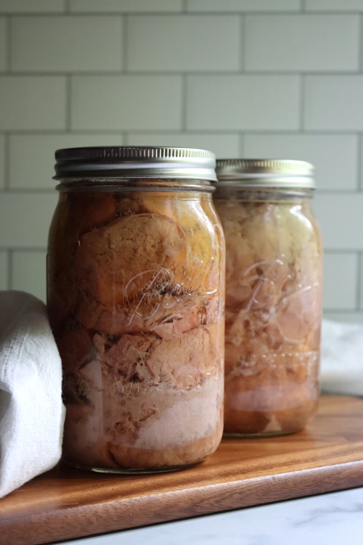 Close-up of two quart jars of pressure canned pork tenderloin on a wooden board