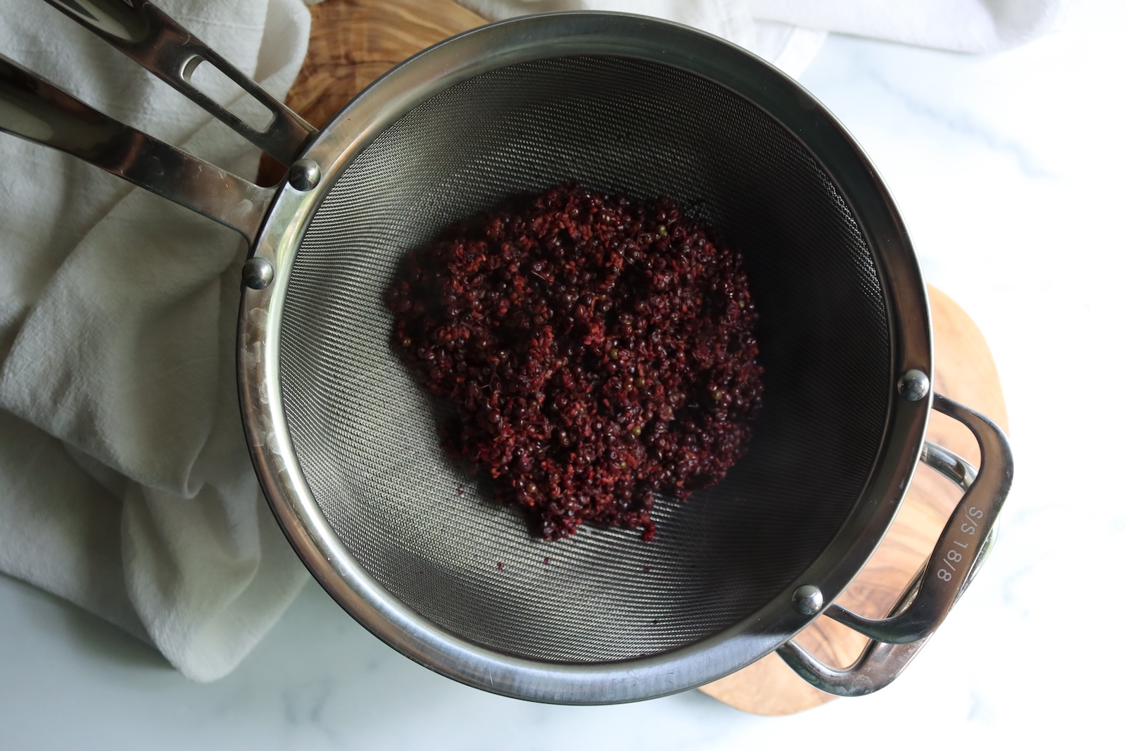 Cooked elderberries draining in a fine-mesh strainer to make elderberry juice