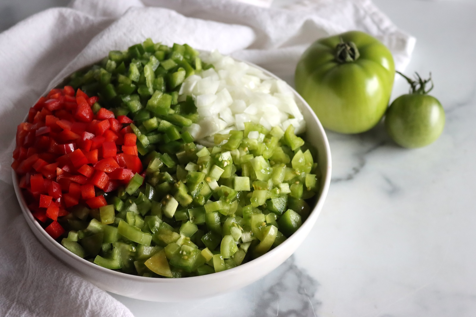 Diced red pepper, green pepper, onion, and green tomatoes in a white bowl