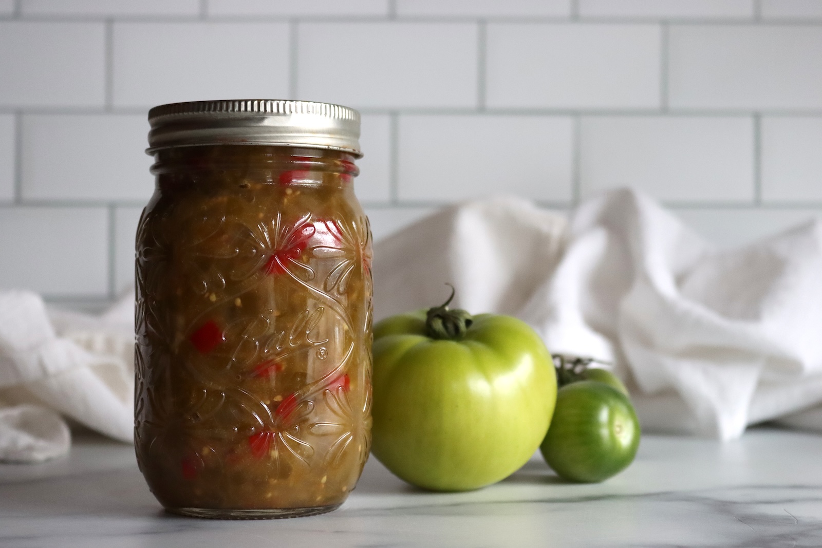 Pint jar of green tomato hot dog relish with green tomatoes behind it