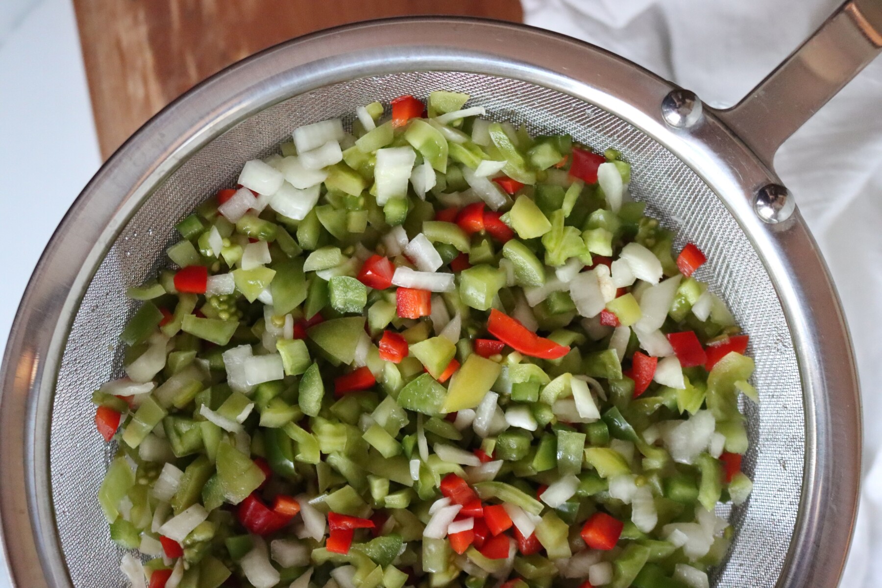 Salted green tomatoes, peppers, and onion draining in a metal strainer