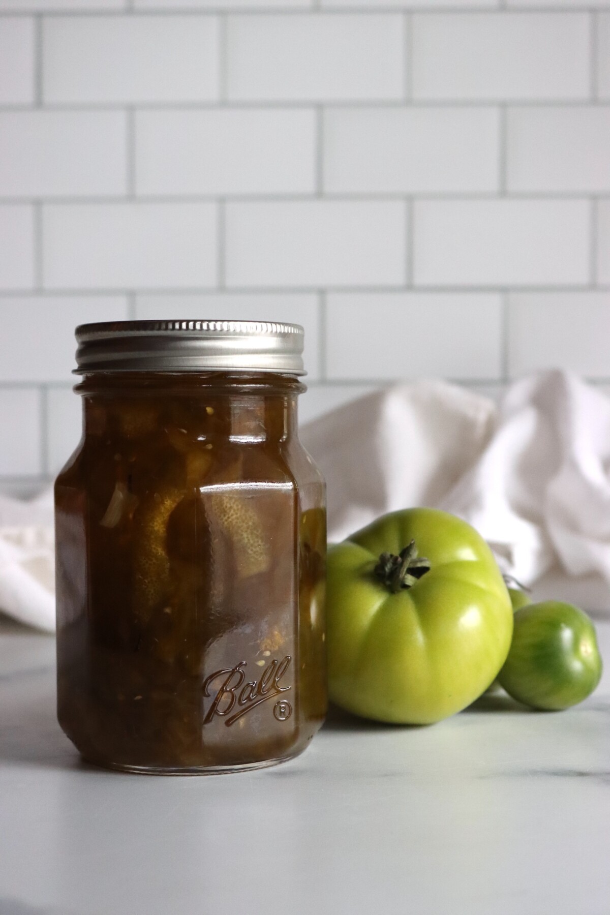 Pint jar of green tomato preserves next to unripe green tomatoes