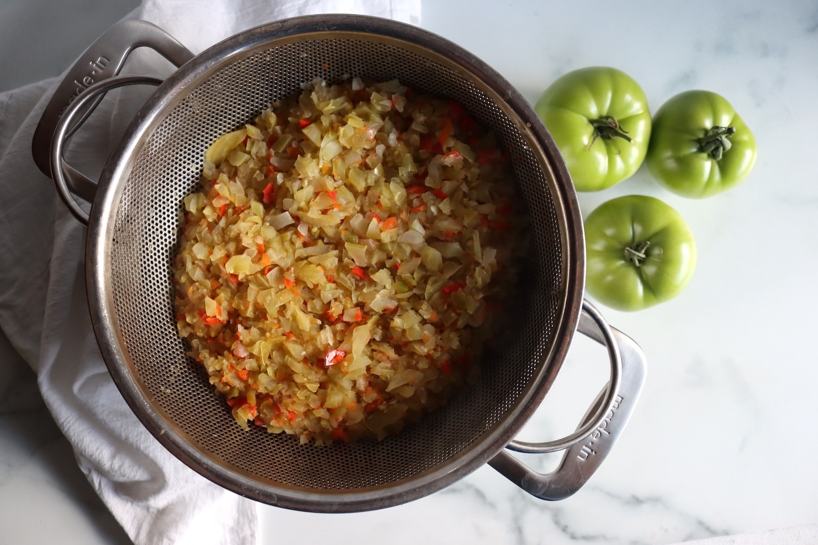 Chopped relish vegetables draining in a stainless steel colander after the salt boil