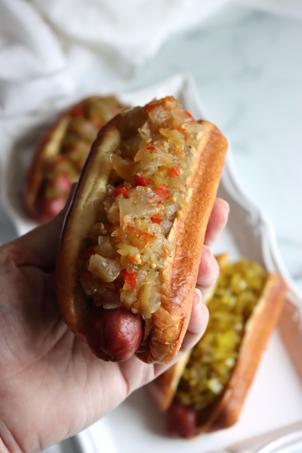 Hand holding a hot dog piled with classic green tomato relish
