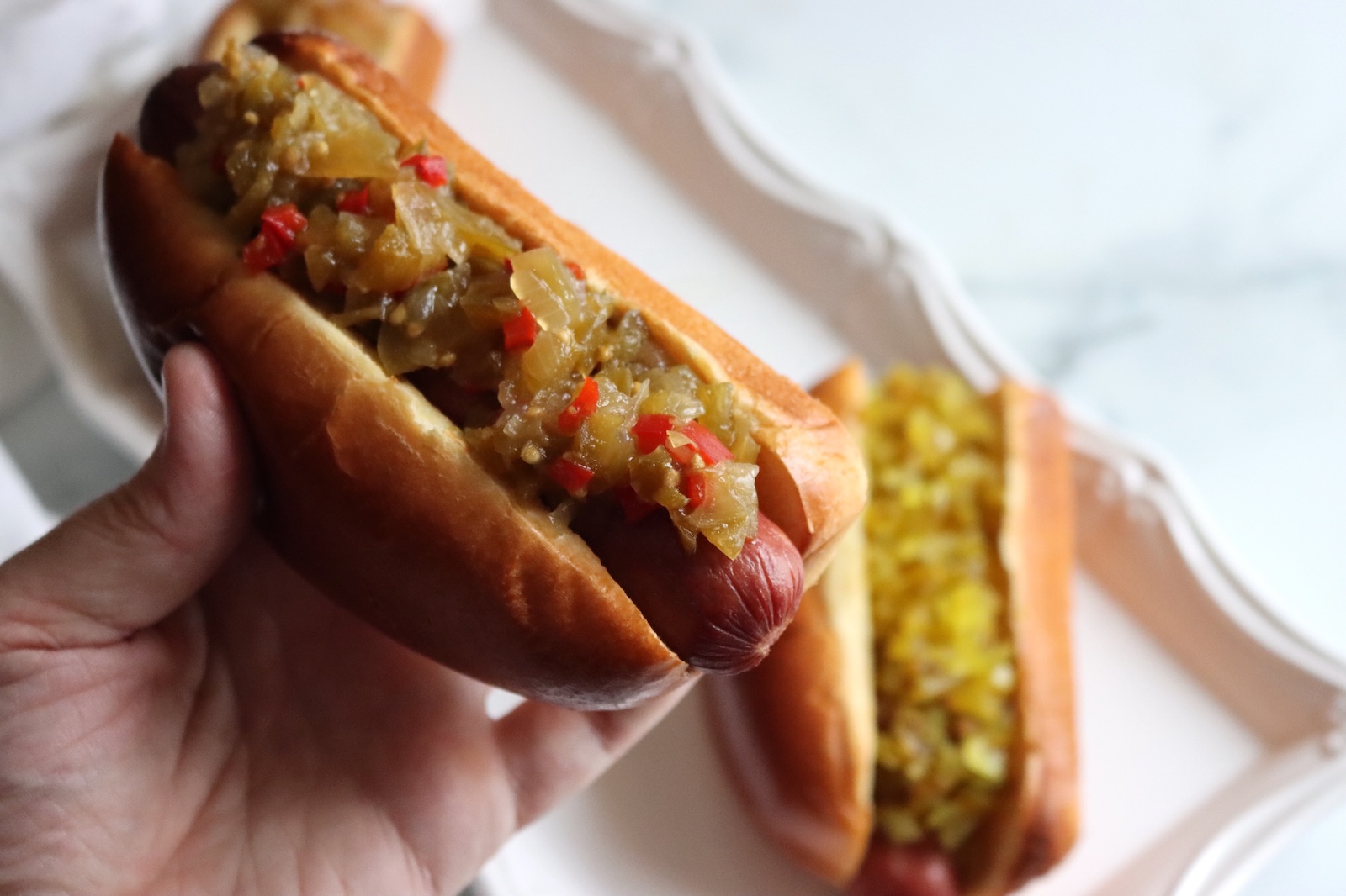 Hand holding a hot dog topped with green tomato hot dog relish