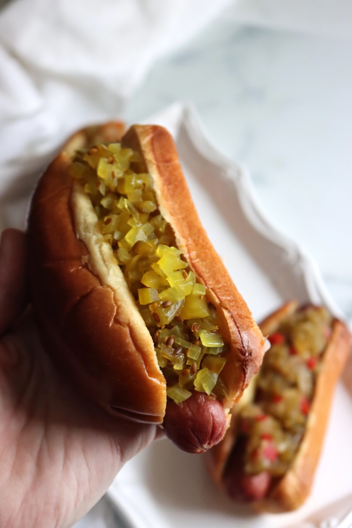 Hand holding a hot dog topped with dilled green tomato relish