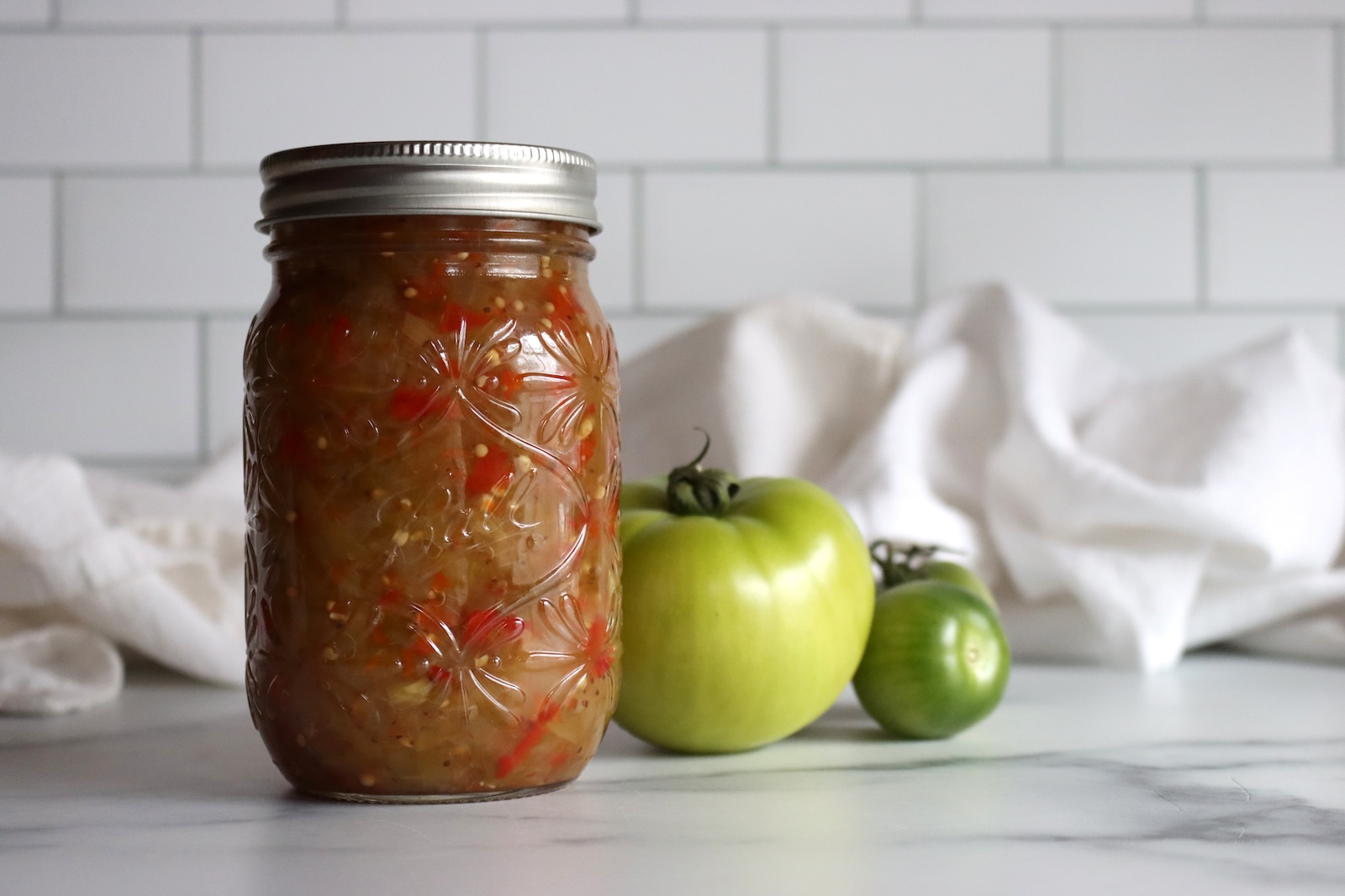 Pint jar of classic green tomato relish with green tomatoes behind it