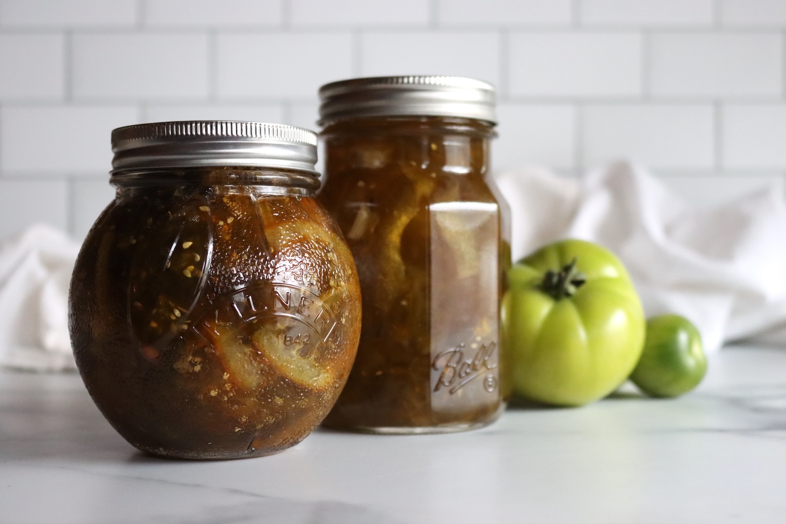 Round jar of green tomato marmalade in front of a pint jar of green tomato preserves