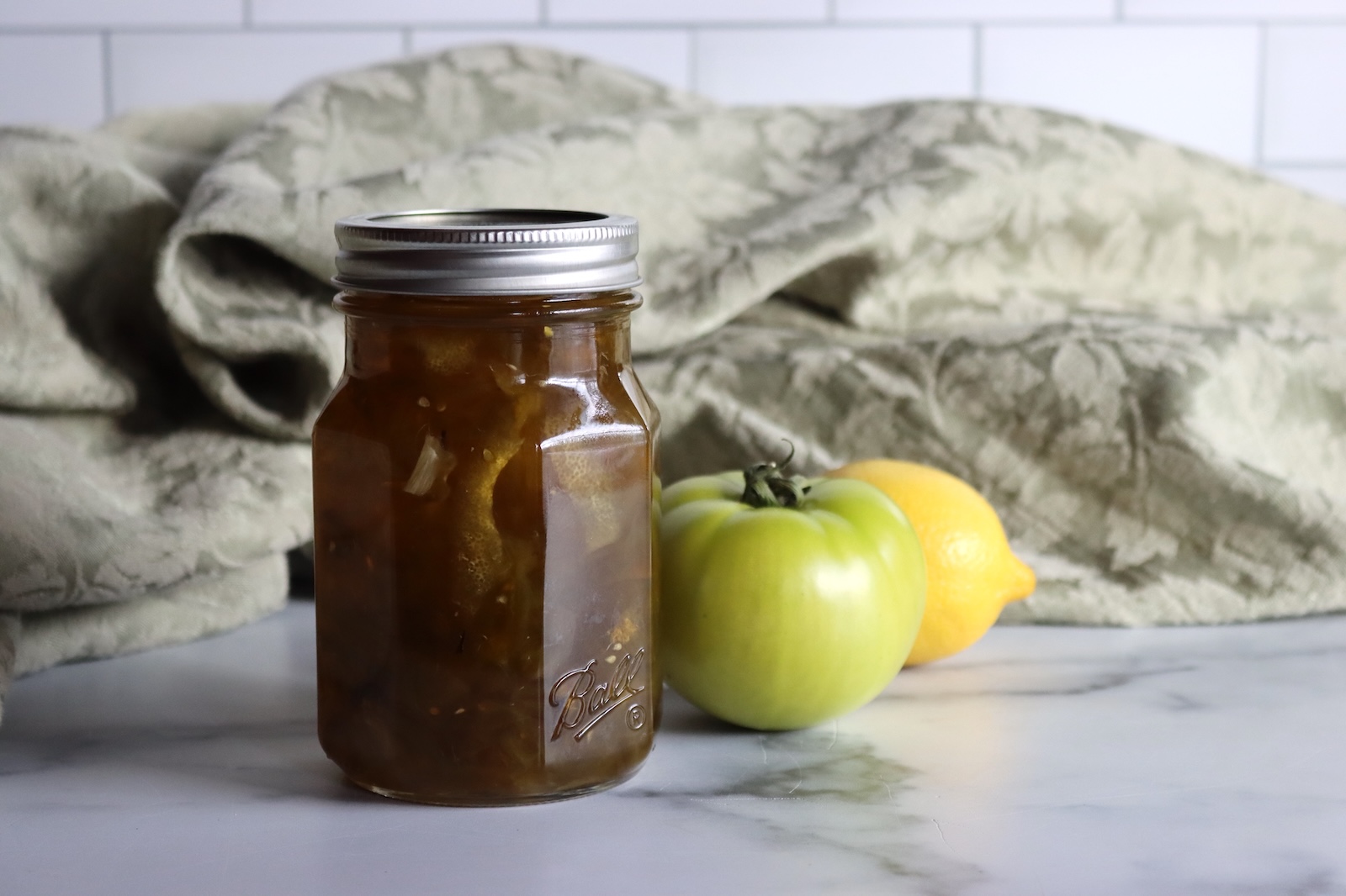Pint jar of green tomato preserves with a green tomato and a lemon
