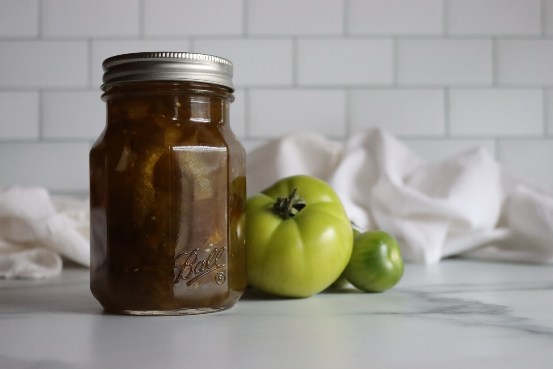 Pint jar of Italian green tomato preserves on a marble counter with green tomatoes
