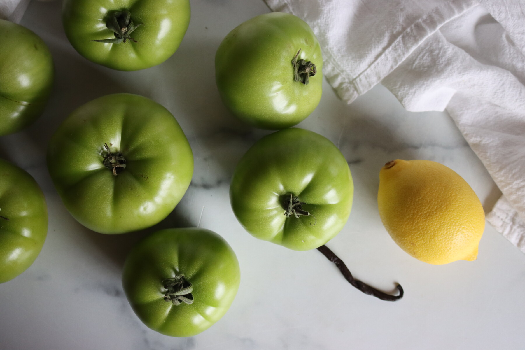 Green tomatoes, a lemon, and a vanilla bean for making Italian green tomato preserves