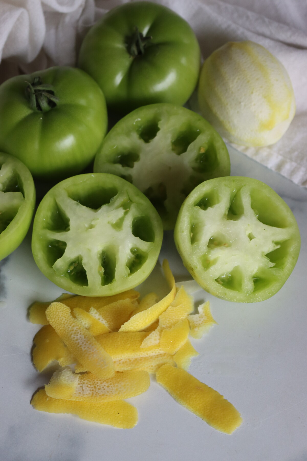 Green tomatoes cut in half to check the seeds, next to strips of lemon peel