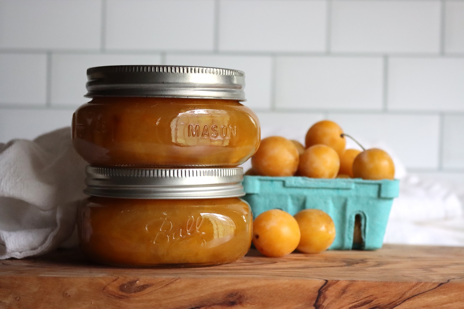Two jars of mirabelle plum jam with fresh mirabelle plums in a berry basket