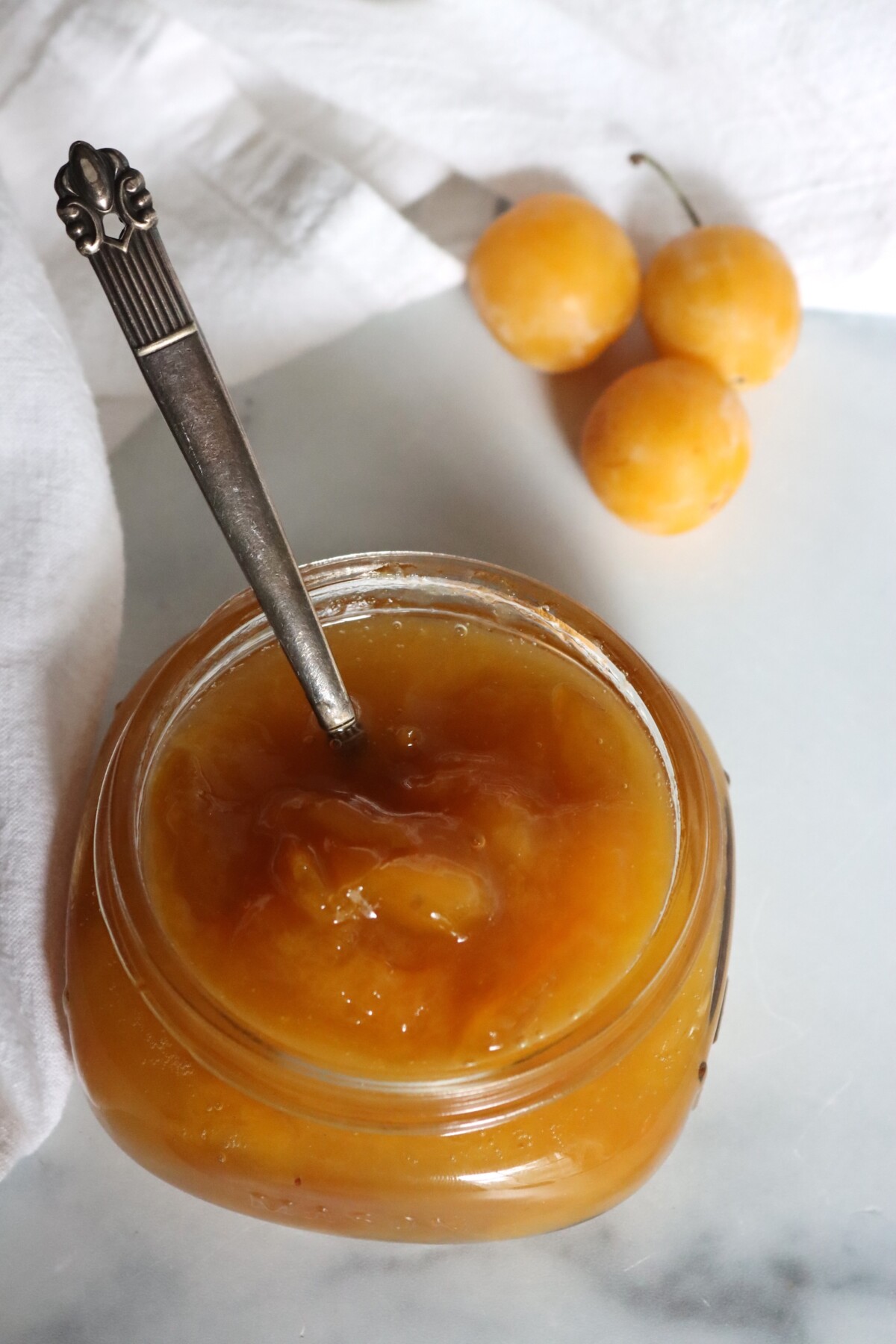 Open jar of mirabelle plum jam with a vintage spoon