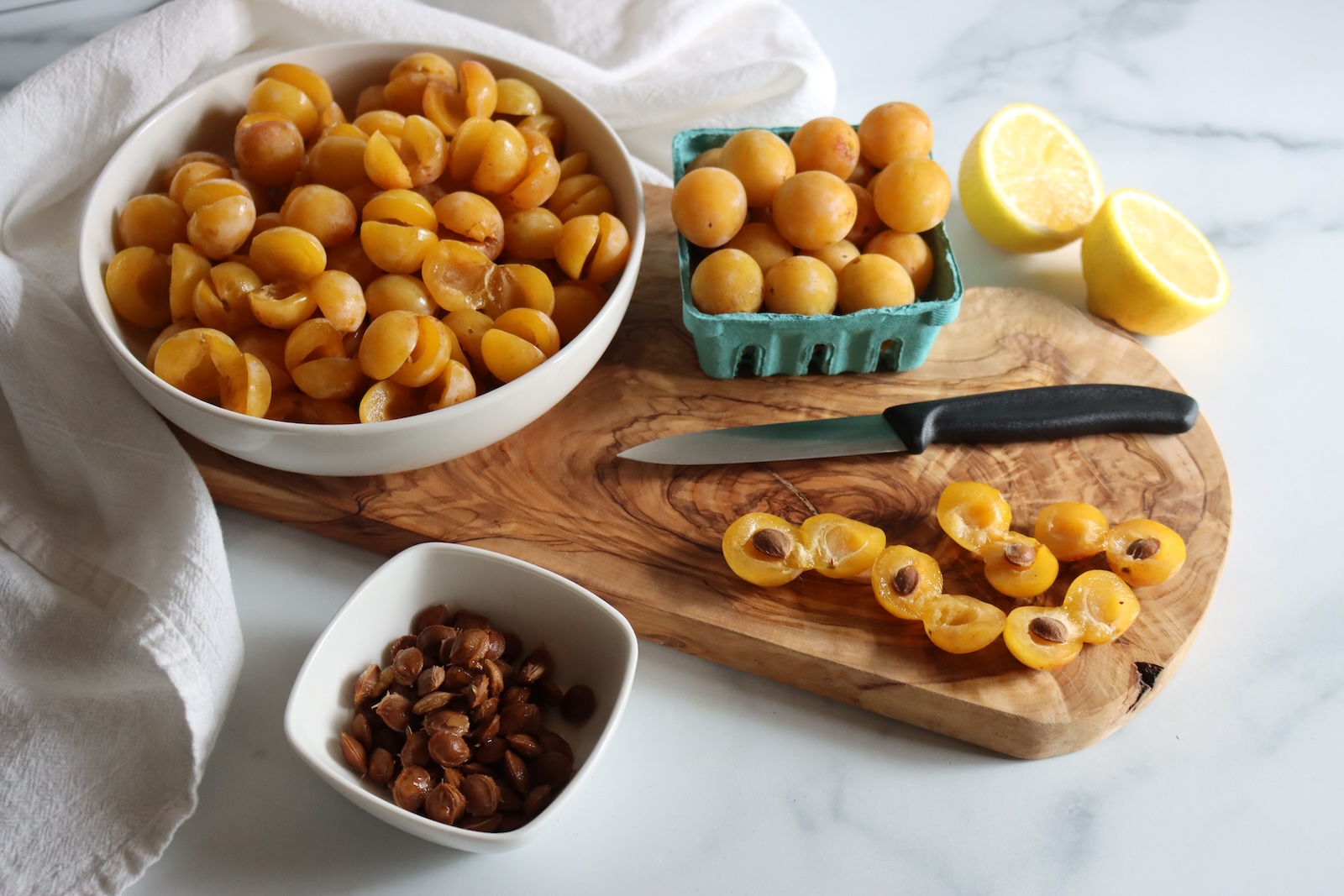 Mirabelle plums sliced in half and pitted, with a paring knife and a bowl of pits
